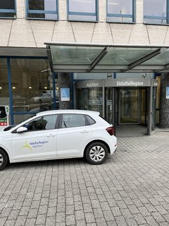 Ein weißes Auto der StädteRegion Aachen parkt vor dem Gebäude der StädteRegion.